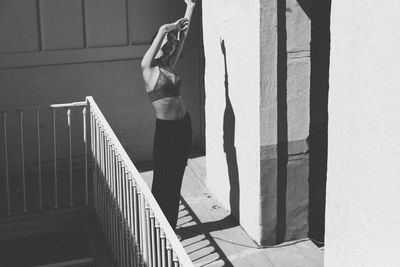 Woman with arms raised standing at balcony during sunny day