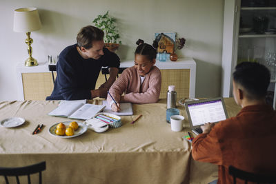 High angle view of gay couple sitting with daughter doing homework while sitting at dining table