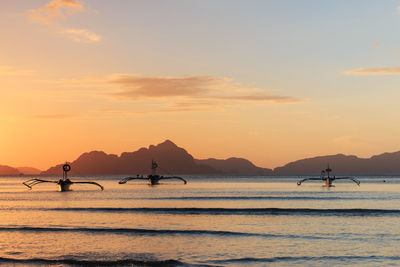 Outrigger boats on sea against sky during sunset