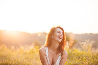 Cheerful woman looking away against sky during sunset