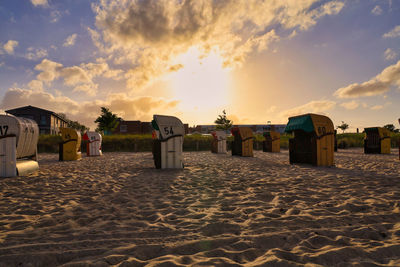 Hooded chairs on beach against sky during sunset