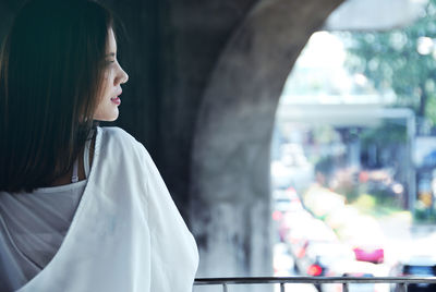 Young woman looking away while standing by railing under bridge