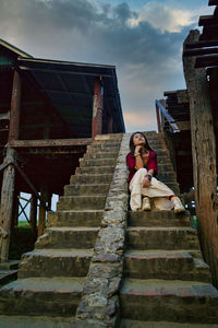 Full length of woman sitting on staircase against sky