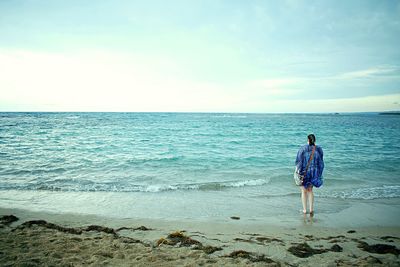 Full length rear view of woman standing on shore at beach