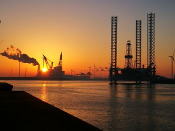 Silhouette cranes in sea against sky during sunset