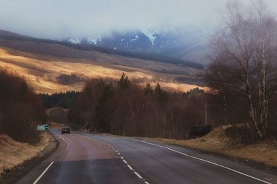 Road by trees against sky