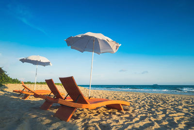 Deck chairs and parasols on beach against sky