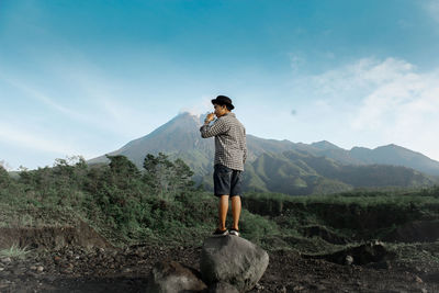 Full length of man standing on rock against mountains and sky