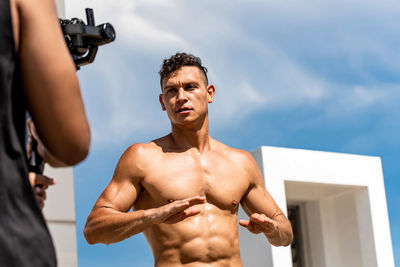 Young shirtless men exercising against sky outdoors