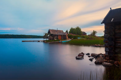 Houses by lake and buildings against sky during sunset