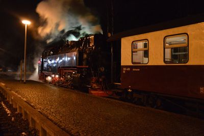 Train on illuminated railroad tracks against sky at night