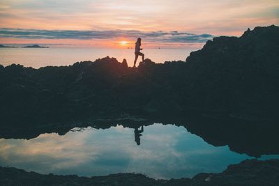 Silhouette woman standing on rock formation during sunset