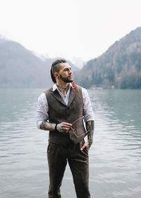 A brutal male hipster groom in a wedding suit in nature by the mountains and lake
