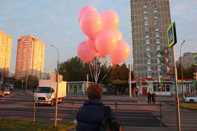 Rear view of man with balloons against buildings in city