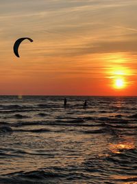 Silhouette people in sea against sky during sunset