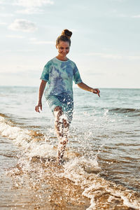 Girl splashing a water towards camera enjoying a free time over sea on a beach at sunset