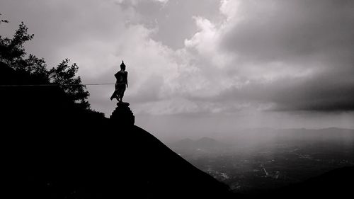 Silhouette man standing on rock against sky