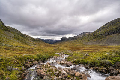 Scenic view of stream amidst mountains against sky