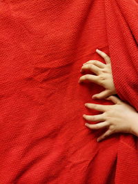 Cropped hands of child on red bed sheet