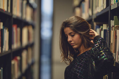 Side view of young woman looking away while standing at library