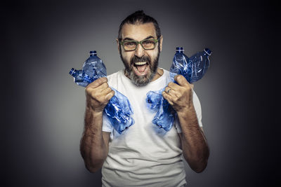 Portrait of man holding plastic bottles screaming against gray background