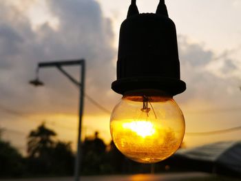 Low angle view of illuminated light bulb against sky at sunset