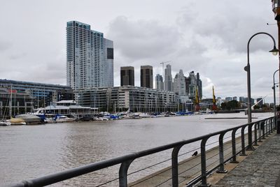 Modern buildings by river against sky in city