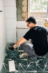 Side view of man sitting on tiled floor