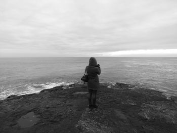 Rear view of woman standing on beach against sky