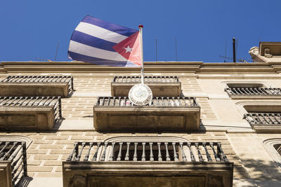 Low angle view of flag against buildings against clear blue sky