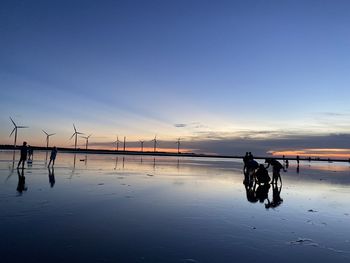 Silhouette people on beach against sky during sunset