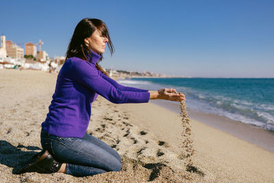 Beautiful happy mature woman playing with the sand on a sunny winter day at the beach