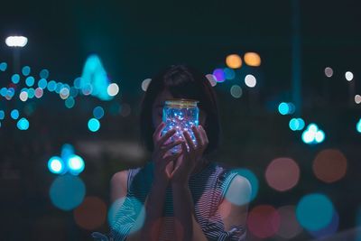 Close-up portrait of woman photographing illuminated smart phone at night