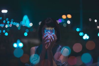 Close-up of woman illuminated string light in jar at night