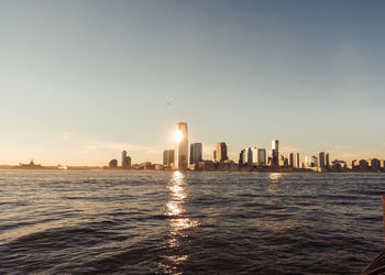 Sea by cityscape against clear sky during sunset