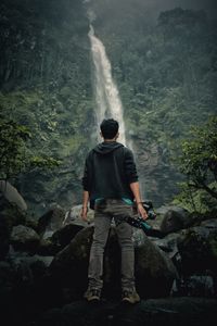 Rear view of man with camera standing against waterfall