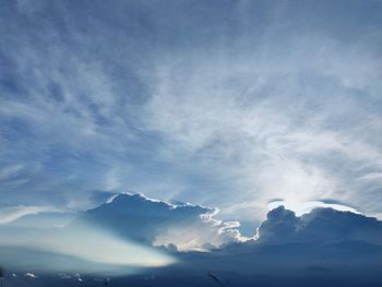 Low angle view of sunlight streaming through clouds