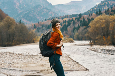 Full length of smiling young woman standing on mountain
