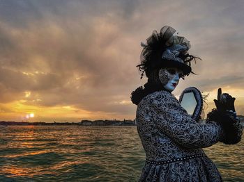 Woman in costume by canal during venice carnival at sunset