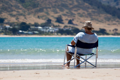 Rear view of woman sitting on chair at beach