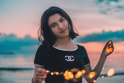 Portrait of smiling young woman standing against sky during sunset