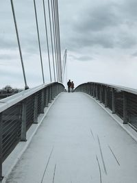 Man walking on footbridge against sky