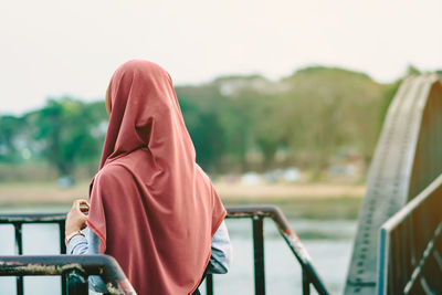 Rear view of woman sitting on railing against sky