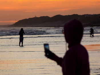 Silhouette man photographing on beach against sky during sunset