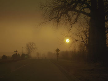 Empty road amidst silhouette trees against sky during sunset