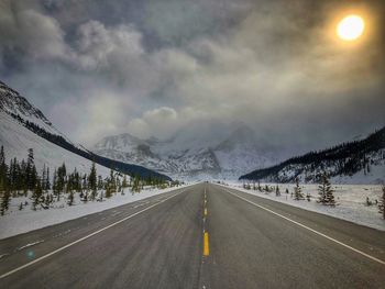 Road leading towards mountains against sky during winter