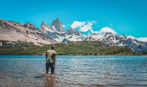 Rear view of man standing on snowcapped mountain against blue sky