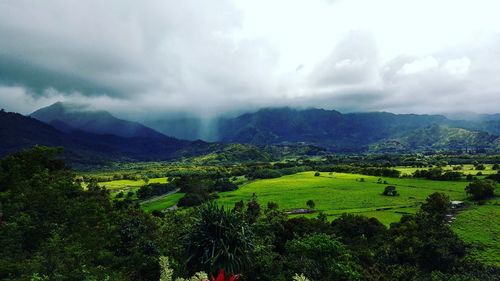 Scenic view of green landscape and mountains against cloudy sky