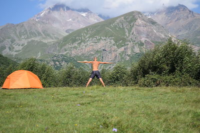 Rear view of man doing yoga in field against mountain
