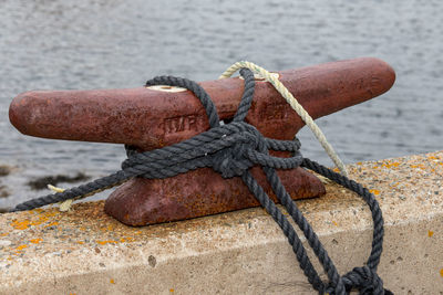 Close-up of rope tied on rusty cleat by sea